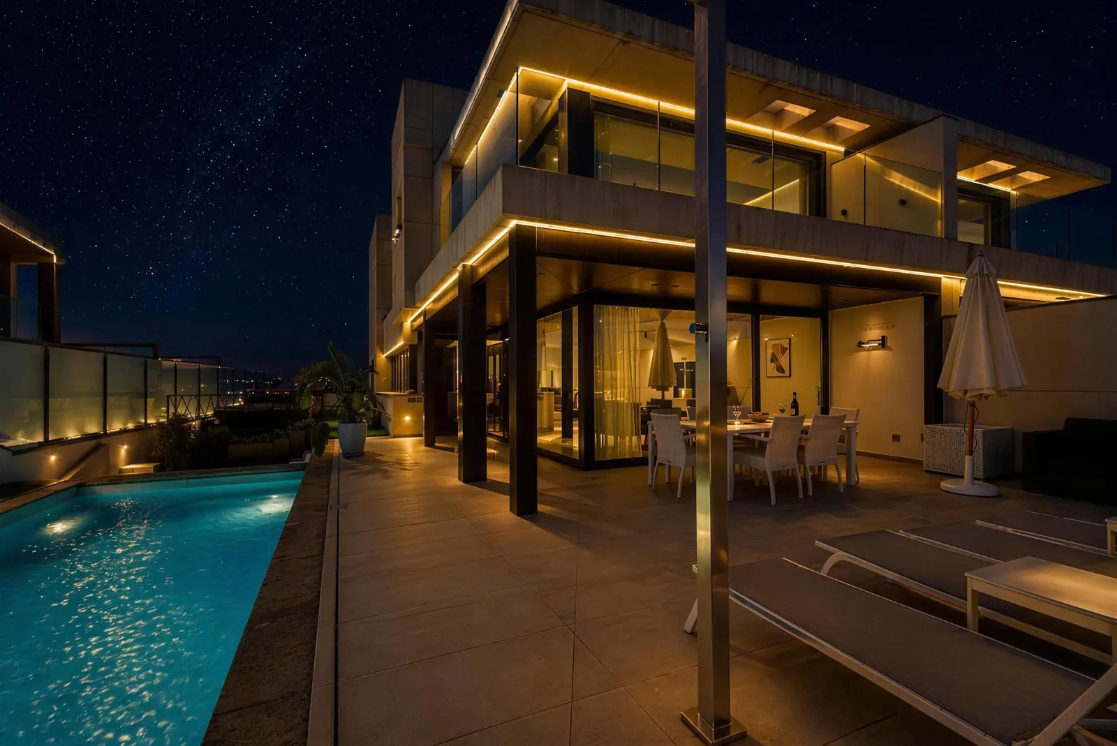 Die Villa bei Nacht mit warmem Licht, überdachtem Essbereich und beleuchtetem Pool