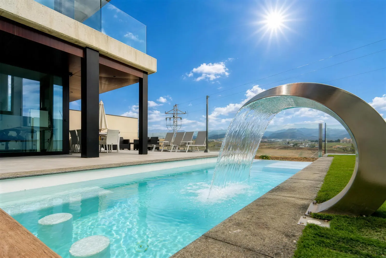 Privatpool mit Edelstahl-Wasserfall, Rasen und Bergen an einem sonnigen Tag