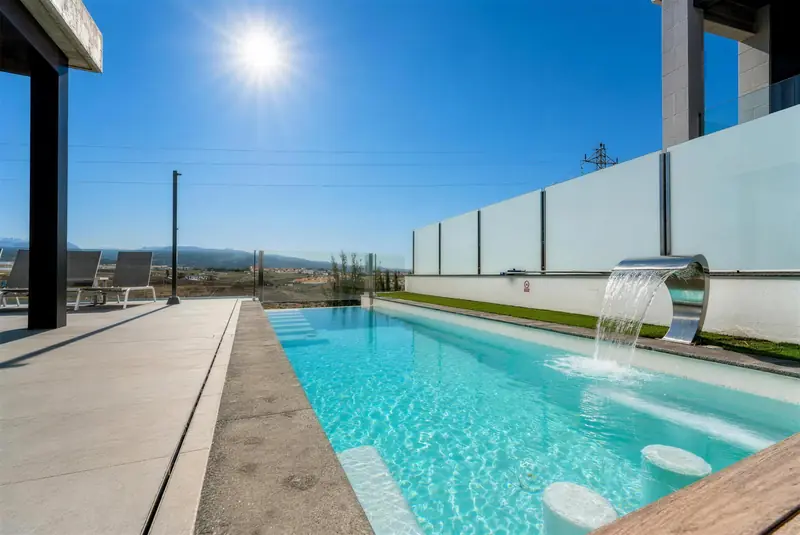 Piscina privada con cascada de acero y asientos dentro del agua, con la montaña al fondo