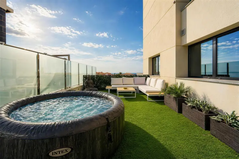 Terraza con jacuzzi, sofás blancos y jardineras